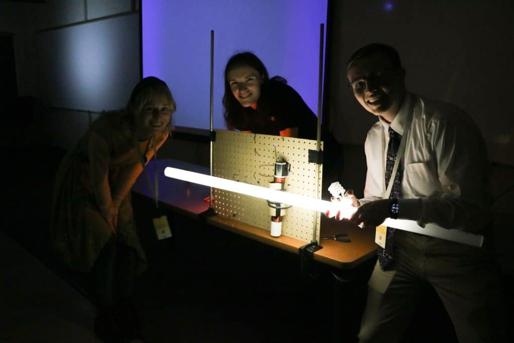 Three people smiling and conducting a light experiment in a dark room.