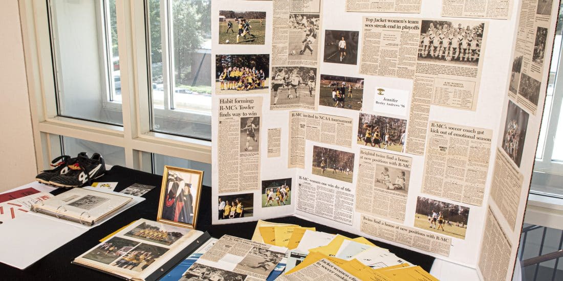 A display featuring a trifold board with newspaper clippings, photographs, and memorabilia highlights the history of journalism. Various documents and photo albums are arranged on a table below the board, capturing the essence of news reporting through the years.