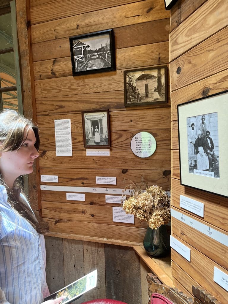 A person examines framed photos, captions, and a bouquet of dried flowers displayed on a wooden wall.