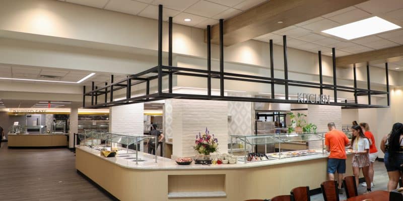 The Renovated Estes Dining servery features a modern cafeteria with a central serving island, where people line up to select their food. The bright lighting, white brick walls, and wooden accents create an inviting atmosphere, setting the stage for the 2024-2025 dining experience.
