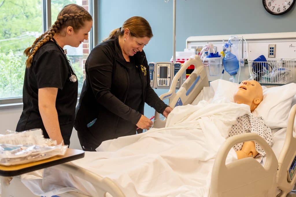 Nursing major Student with professor at bedside of medical mannequin in Payne Hall