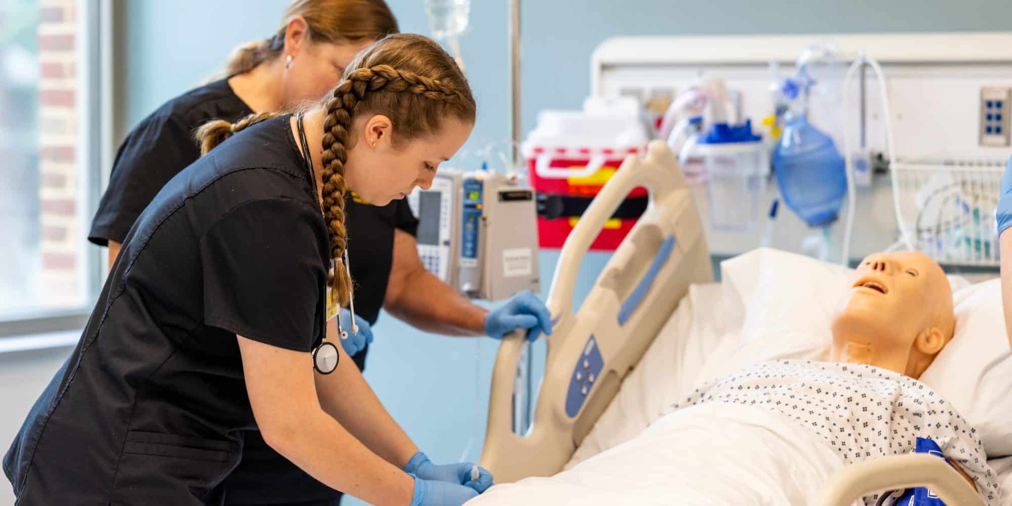 Nursing major with professor using medical mannequin at bedside