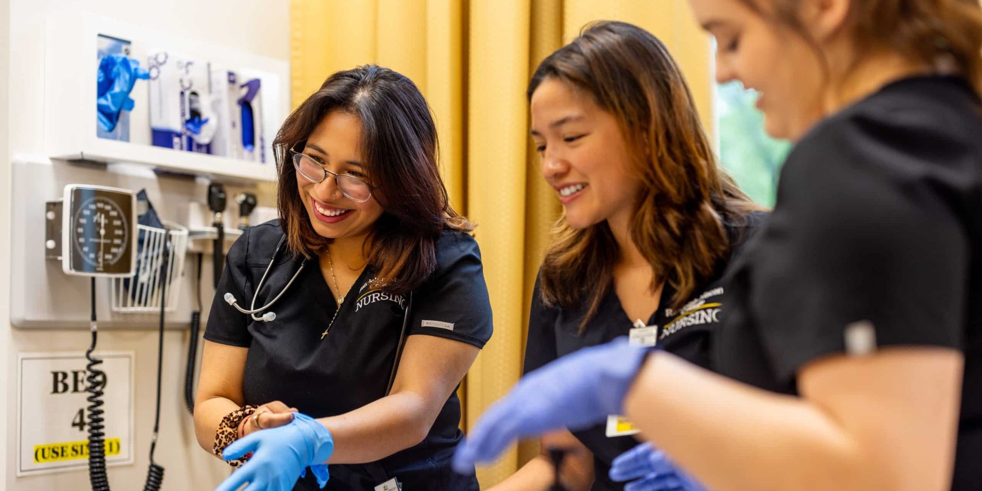 Three nursing students with gloves standing near a bedside