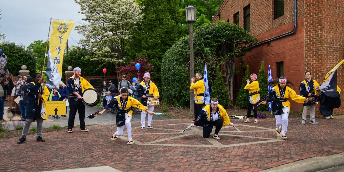 A group of people in traditional clothing perform a coordinated dance with instruments and banners on a brick walkway, capturing the essence of Japanese Studies.