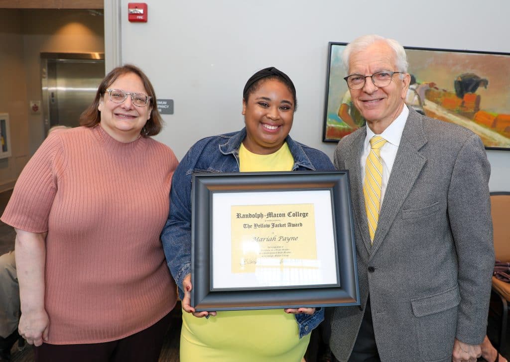 Three people smiling, one holding a framed Randolph-Macon College award.