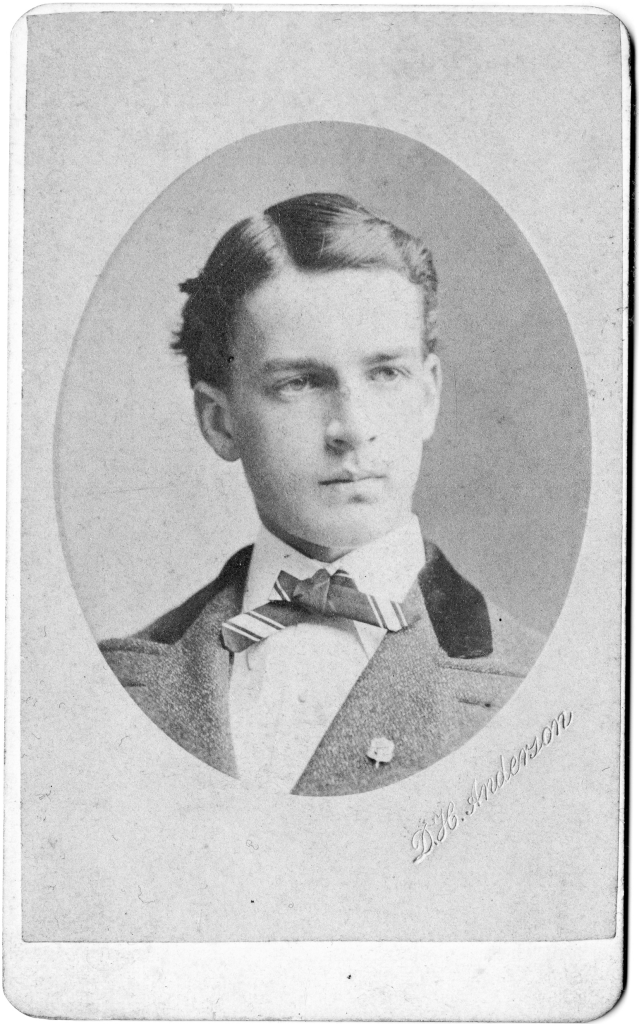 Vintage portrait of a young man in a suit with a bow tie, featuring a formal hairstyle.