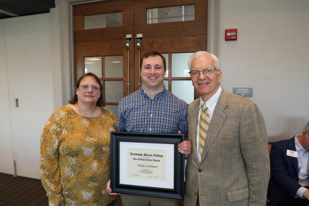 Three people stand indoors; the middle person holds a framed certificate from Randolph-Macon College.