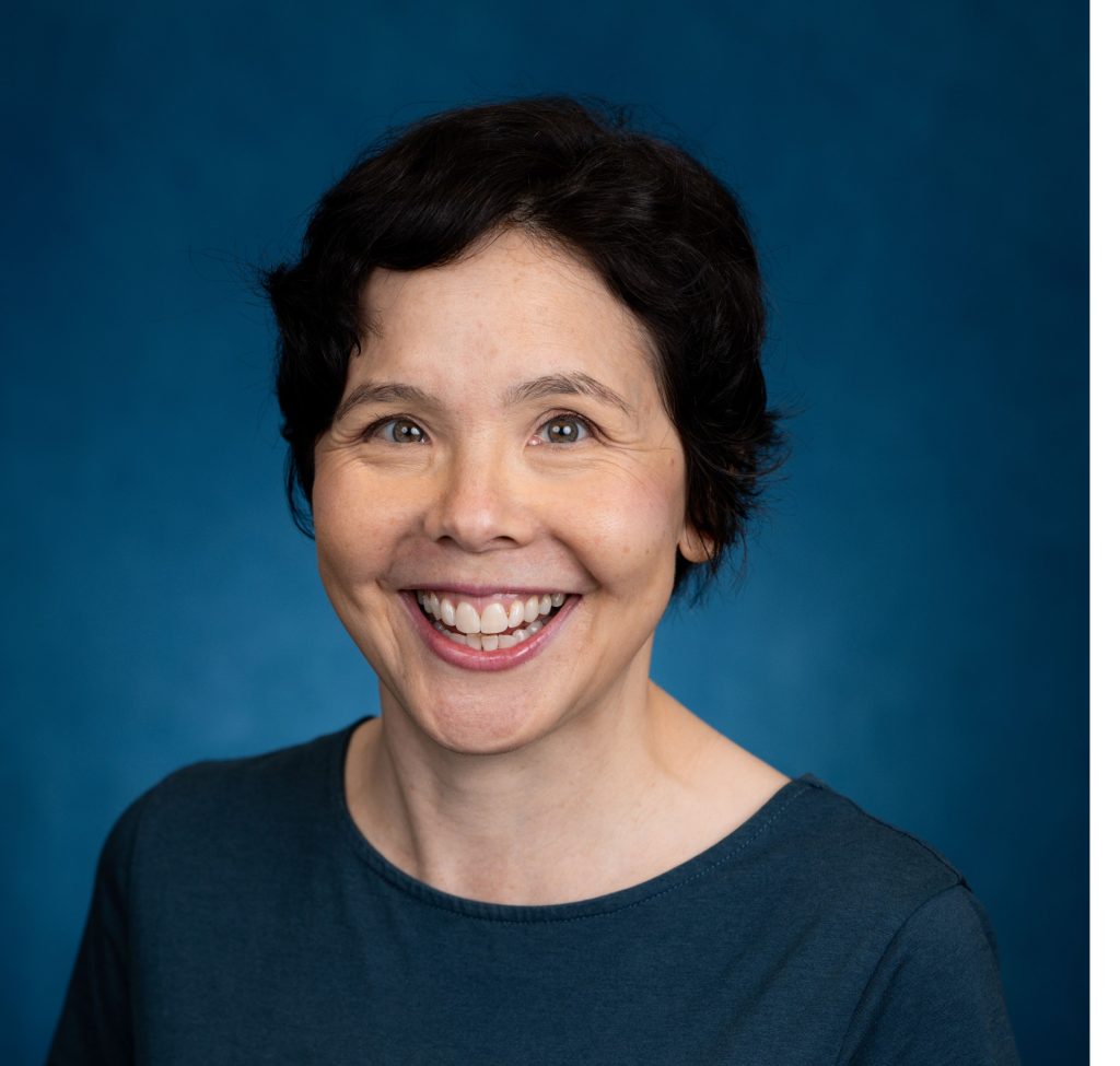 Miranda Brown is smiling warmly at the camera against a vibrant blue backdrop.