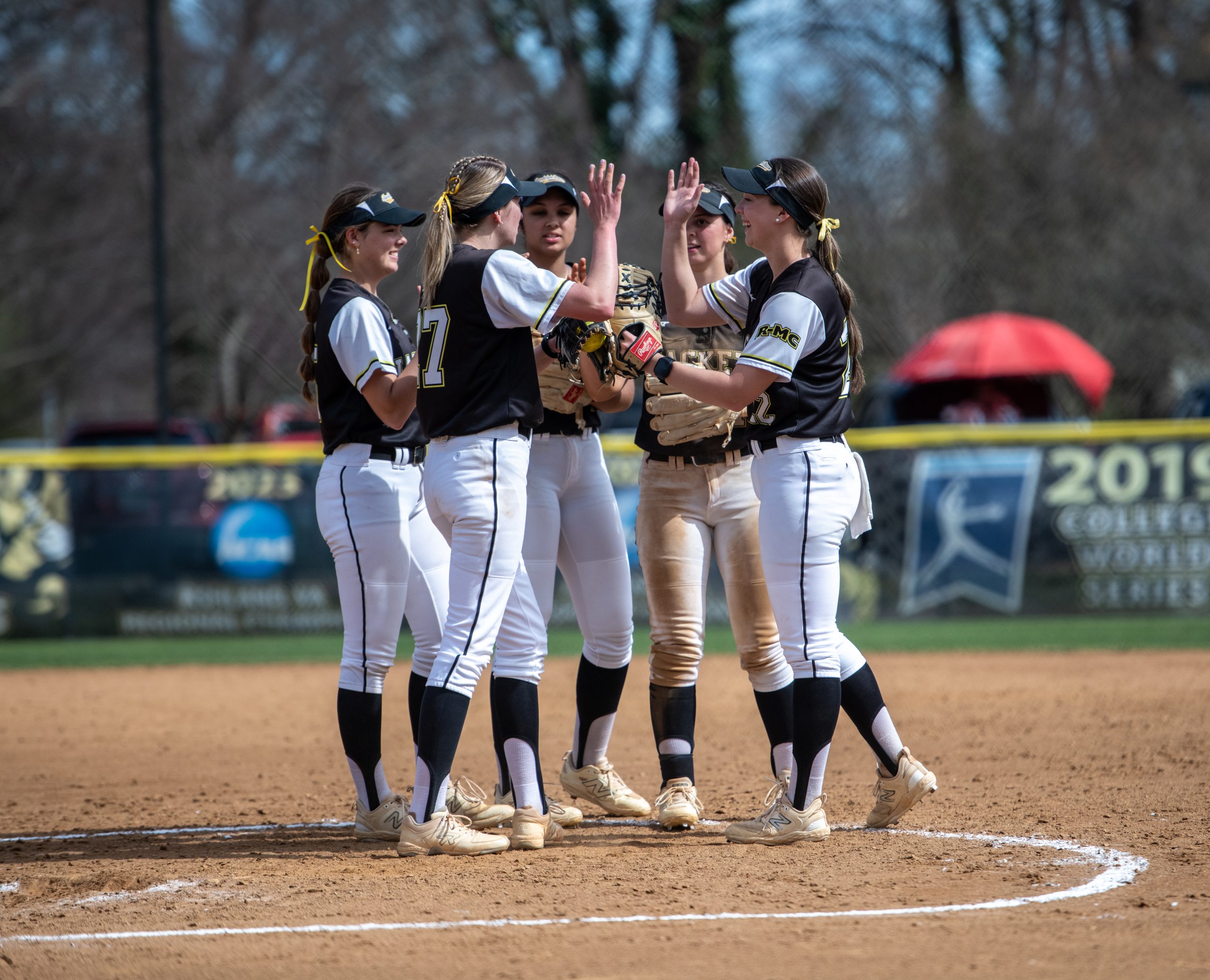 Five RMC softball players stand in the pitcher's circle giving high-fives.