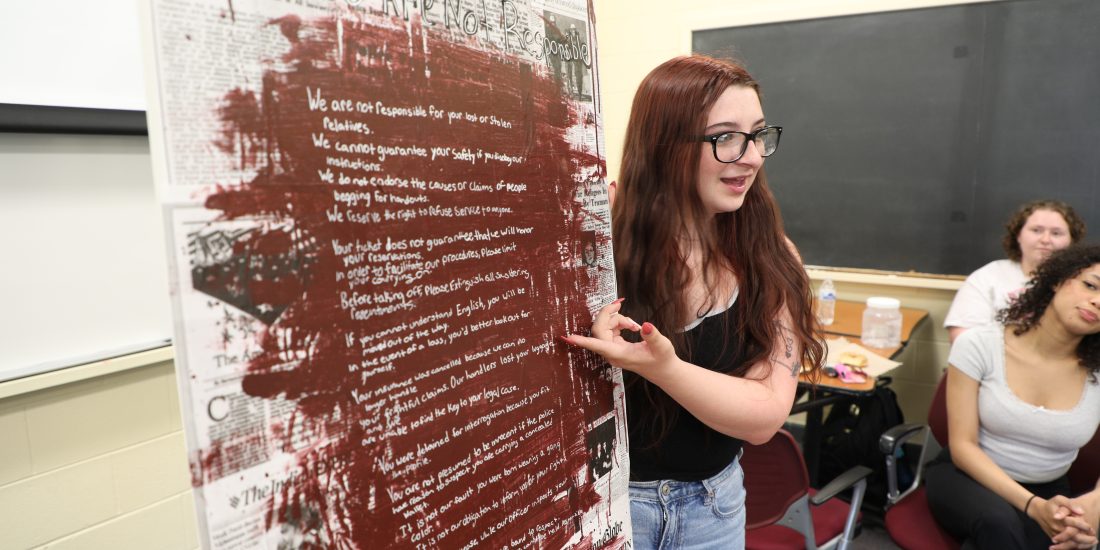 An individual presents a handwritten poster with red markings to a small group in a classroom.
