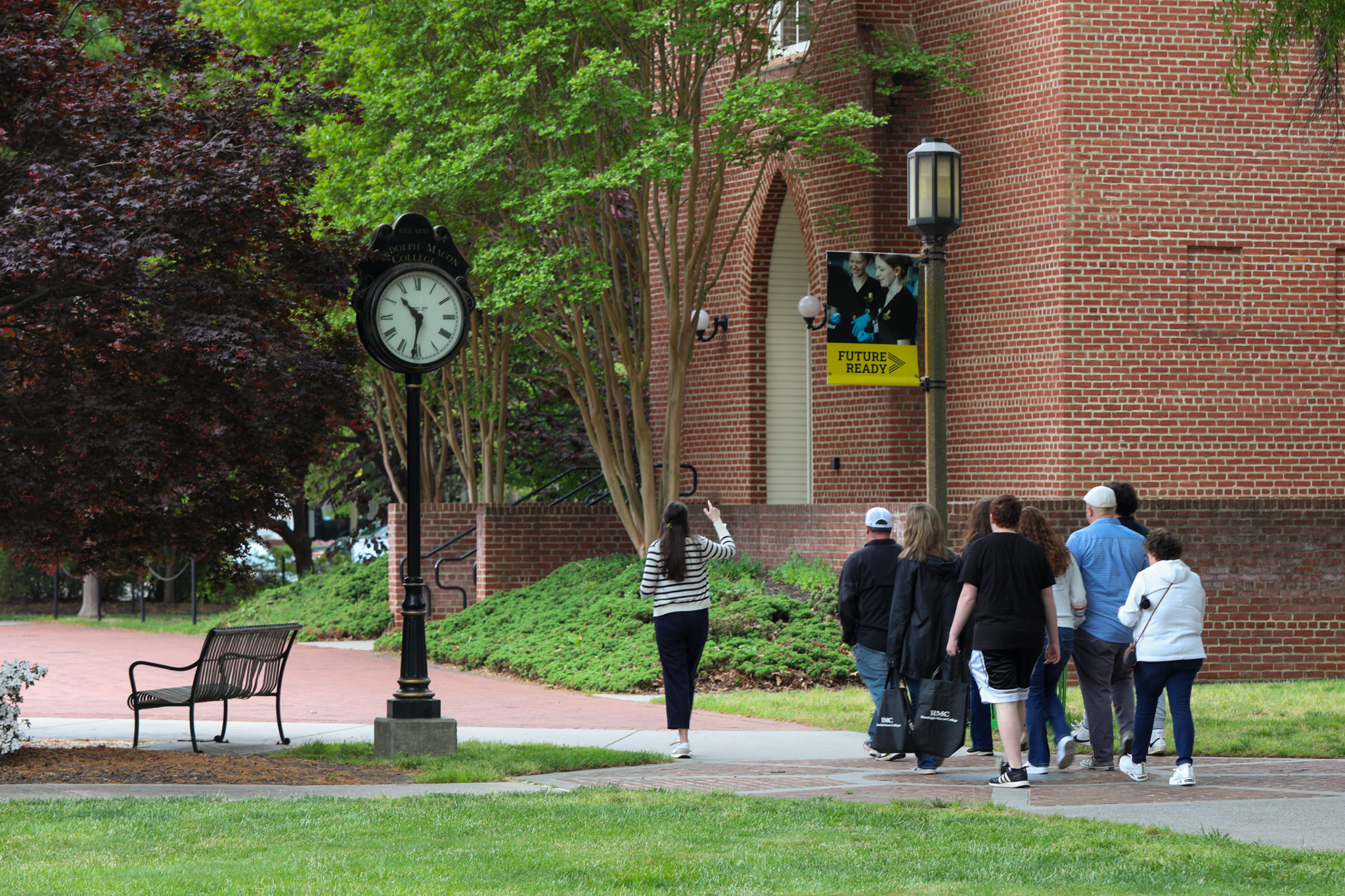 A group walks along a campus path near a brick building and clock.