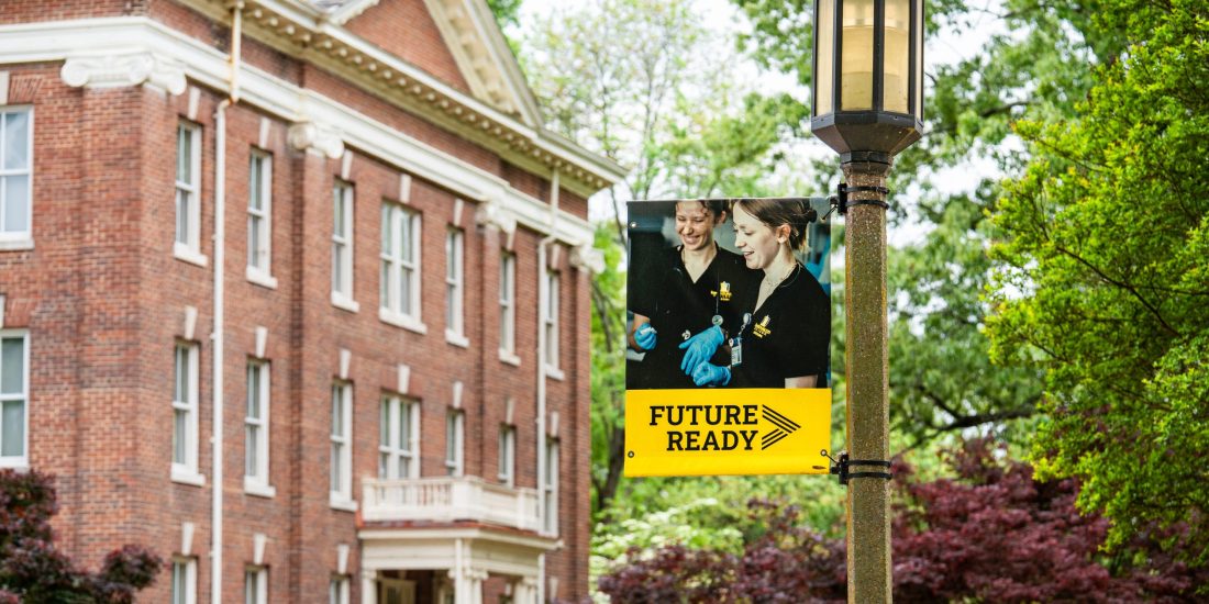 A banner reading "Future Ready" hangs from a lamppost on campus, with an academic building and trees in the background.