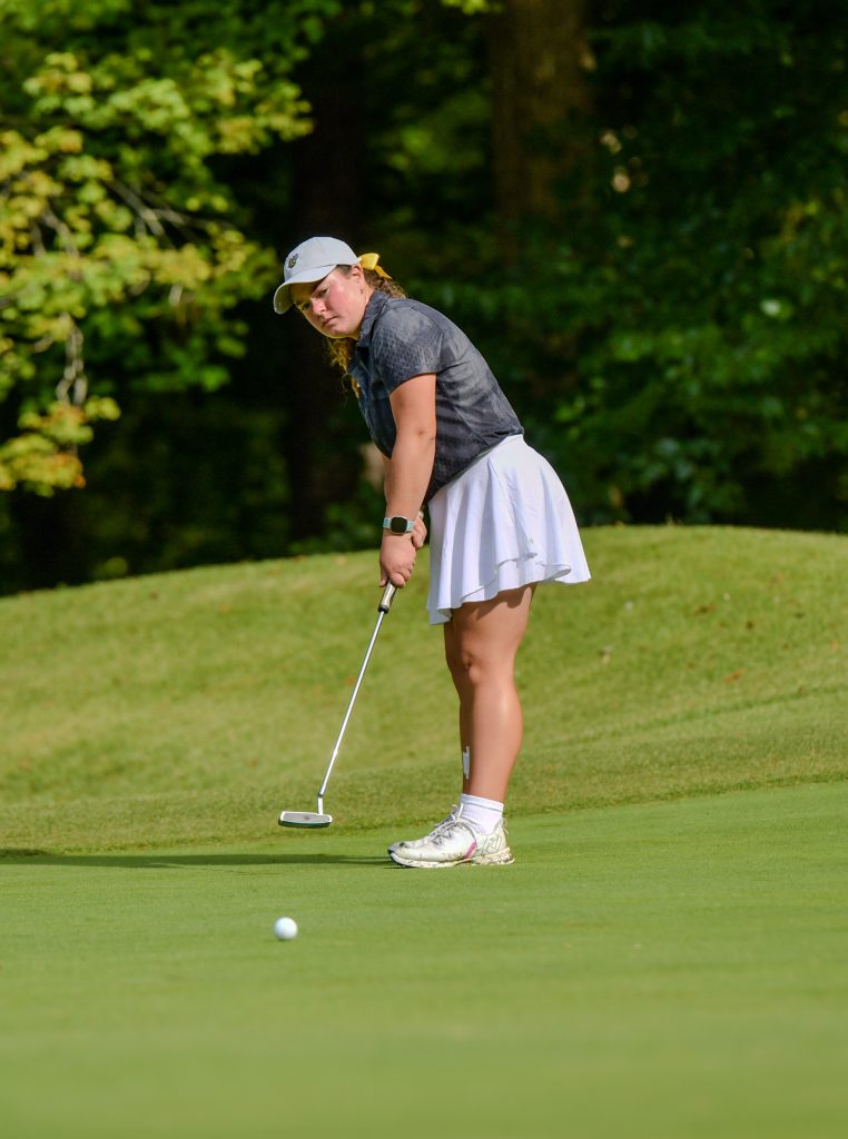 A golfer putts on a green, watching the ball roll toward the hole.