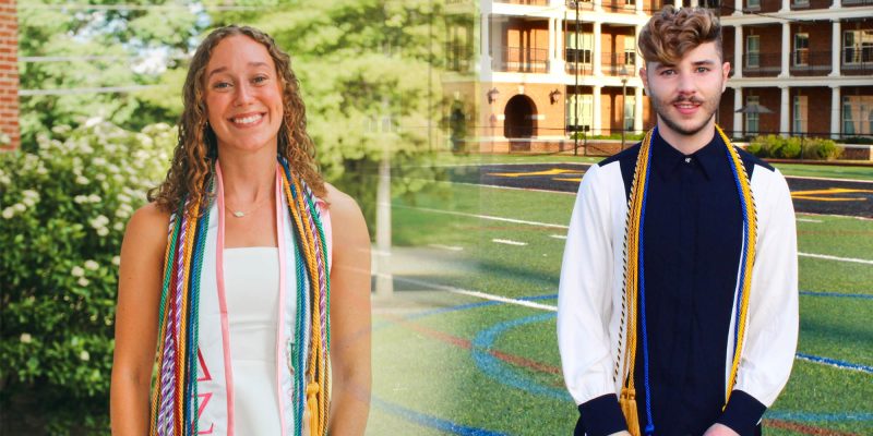 Two graduates with honor cords stand outdoors, one near greenery and the other by a sports field and building.
