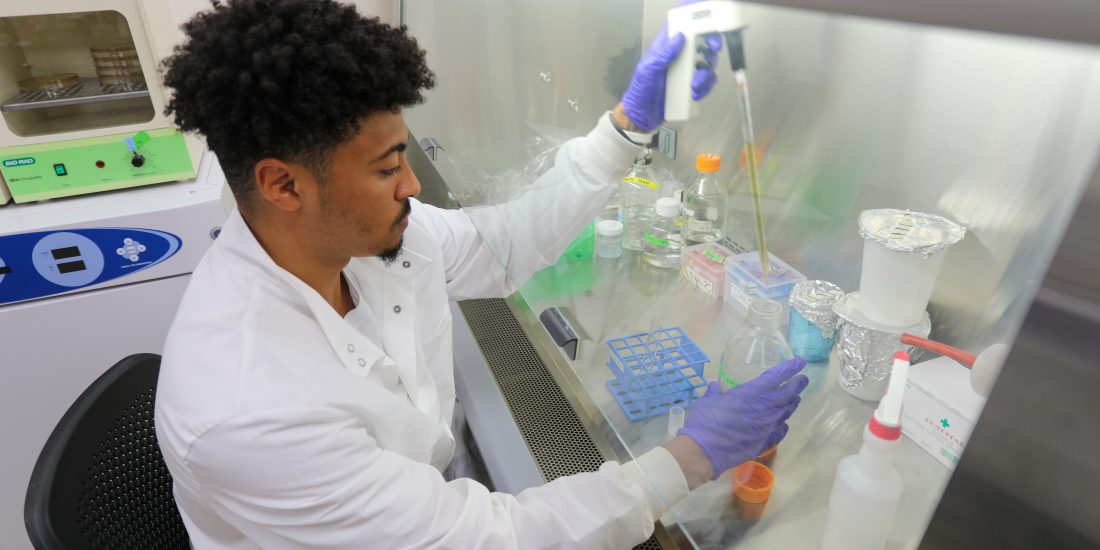 An RMC student sits in a lab and uses a pipette to transfer liquid into a beaker.