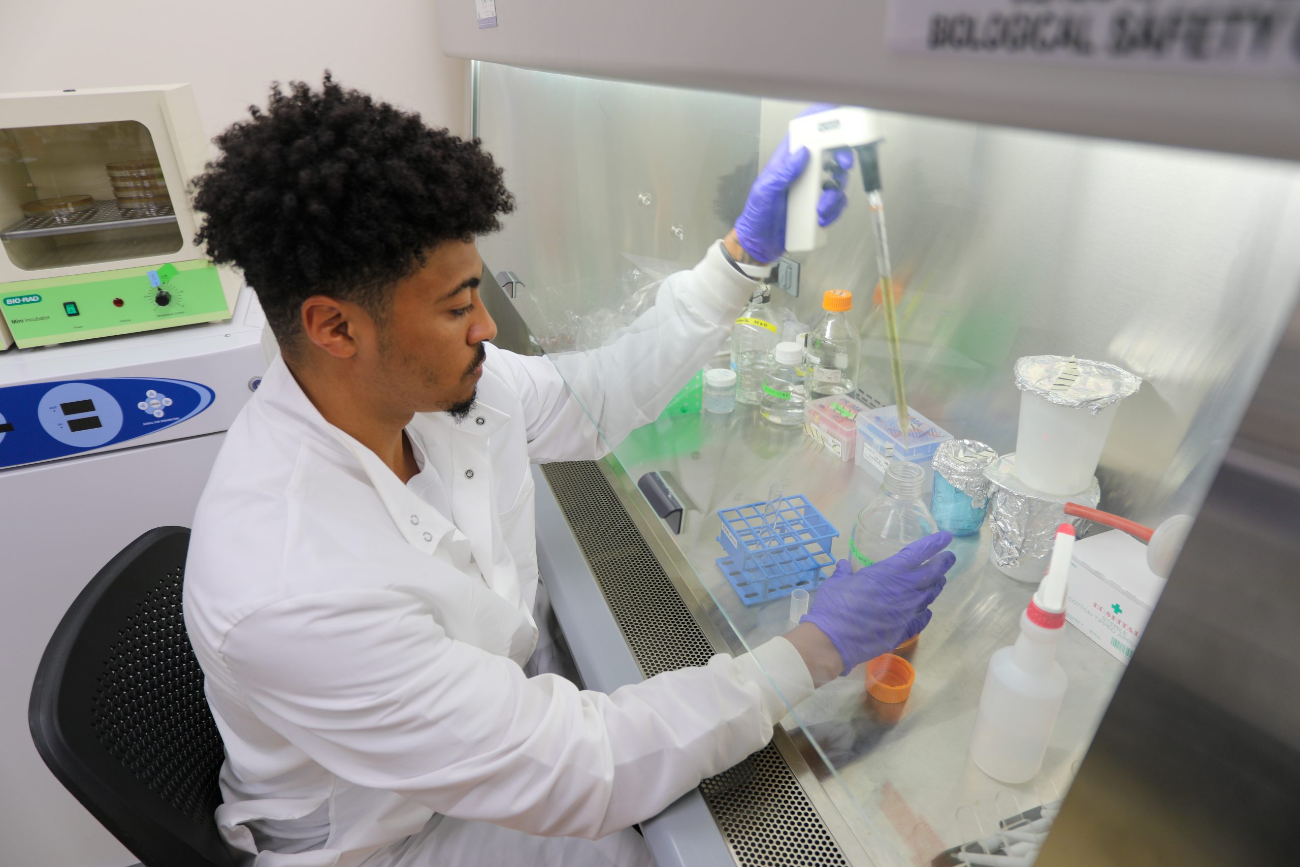 An RMC student sits in a lab and uses a pipette to transfer liquid into a beaker.