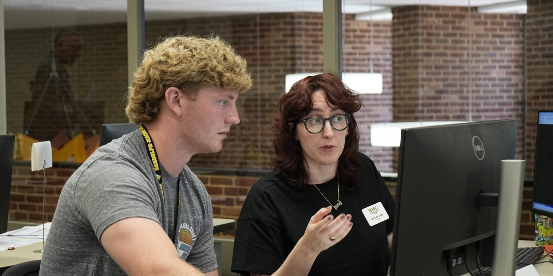 Student and professor sit at computer together.