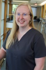 Ashley Foster, MSN, RN, stands indoors in a brightly lit room with large windows and modern furnishings.