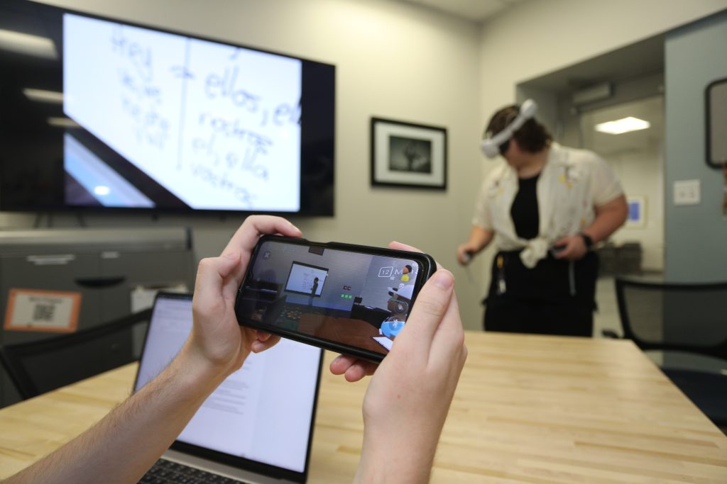 A smartphone displays an augmented reality interface as another individual uses a VR headset in an office environment.