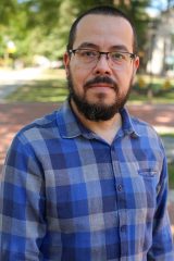 Urani Montiel stands outdoors on a sunny day, with trees and a path in the background.