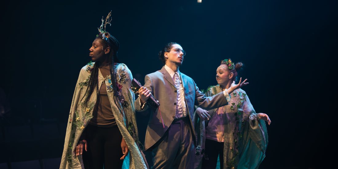 Three performers on stage in dramatic lighting.