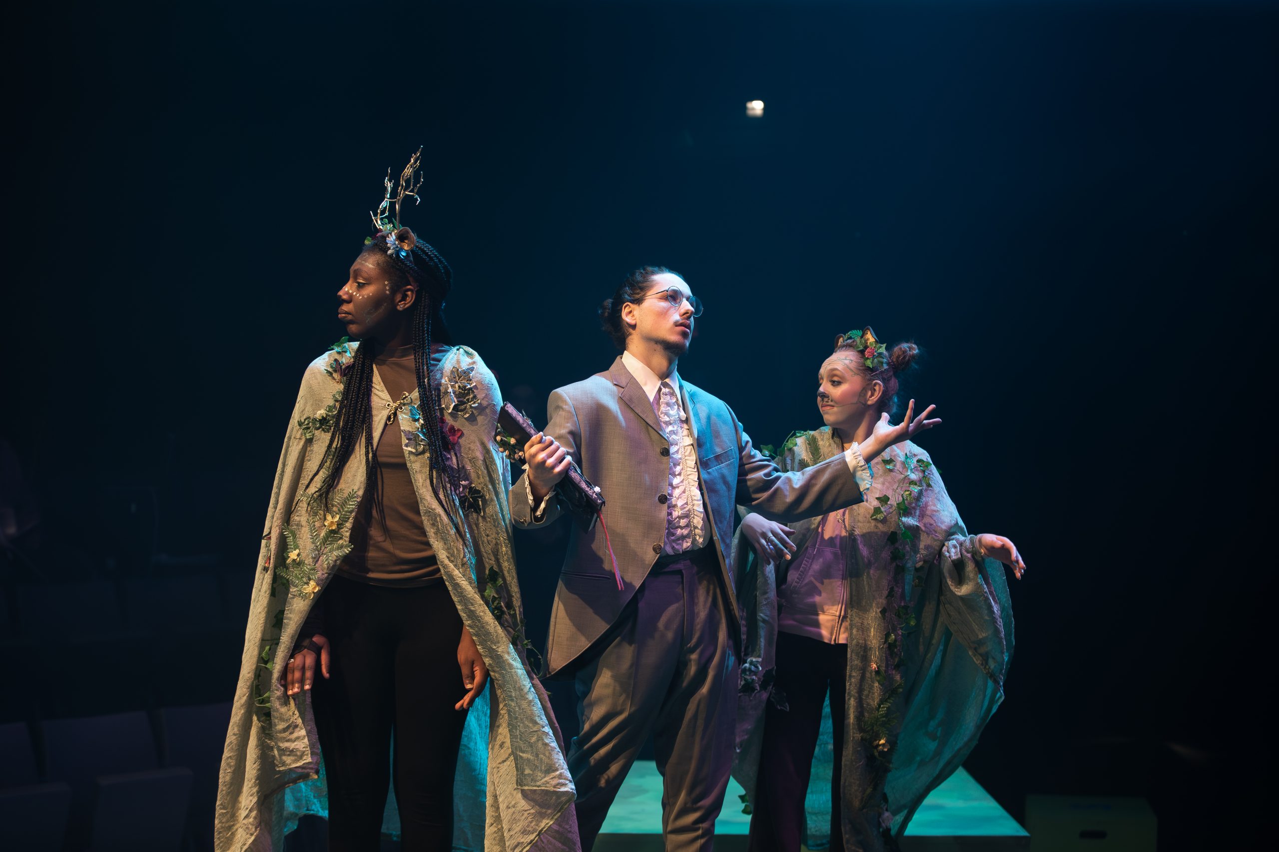 Three performers on stage in dramatic lighting.