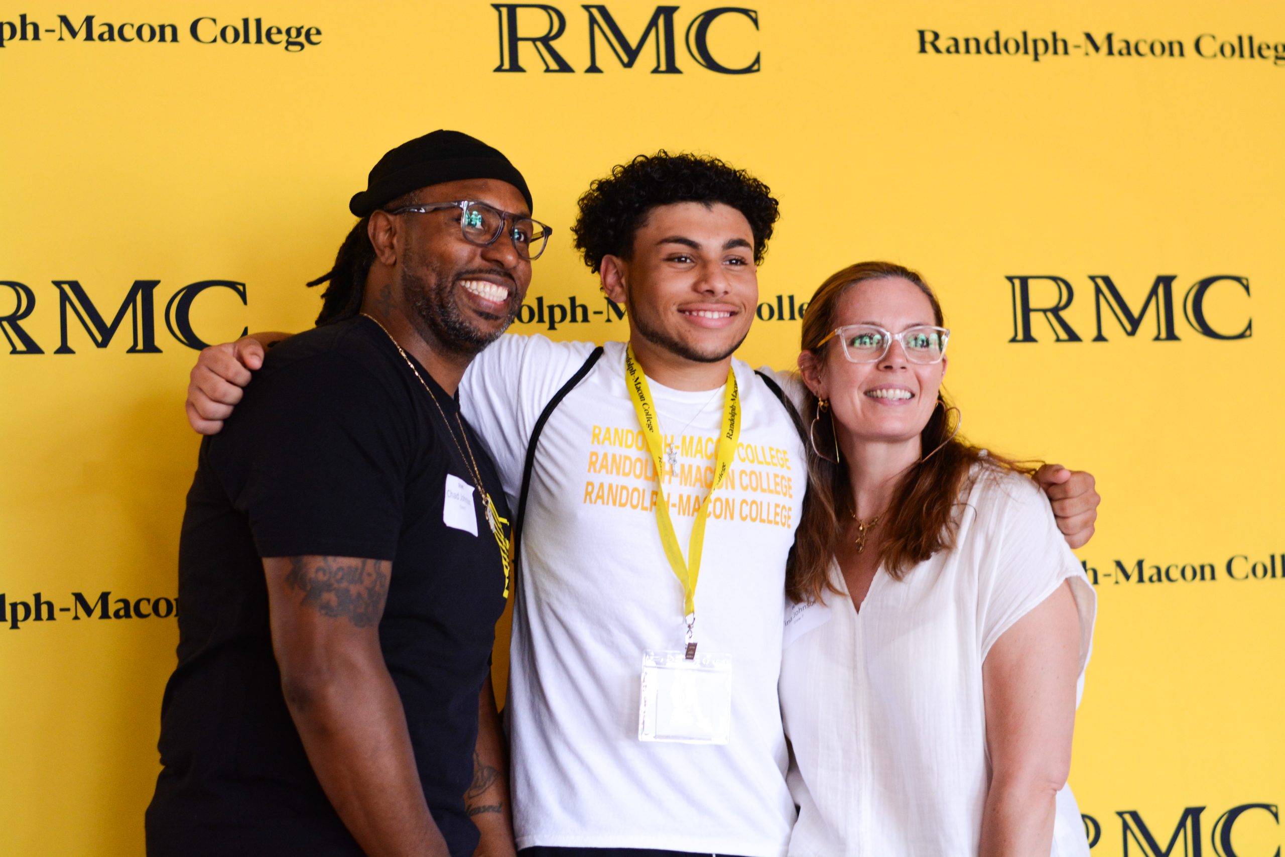 Three people smile in front of a yellow Randolph-Macon College backdrop.