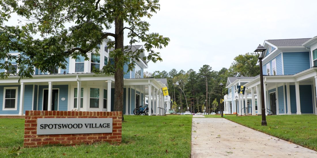 Sidewalk running through Spotswood Village with blue buildings, grassy areas, and trees.