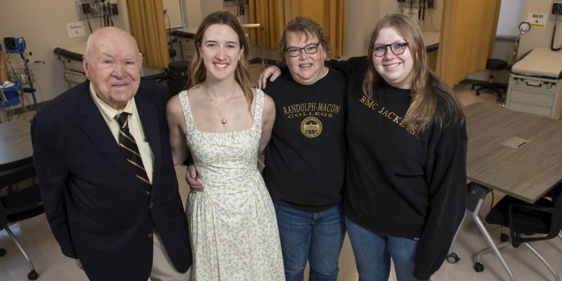 Four people stand together in a medical classroom setting, smiling at the camera.