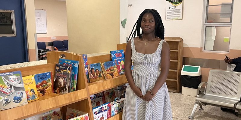 An individual stands beside a children's book and toy display in a brightly lit waiting area with chairs and posters on the wall.