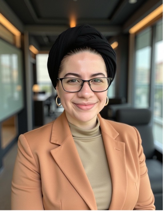 An individual smiles while seated in a modern office with large windows.