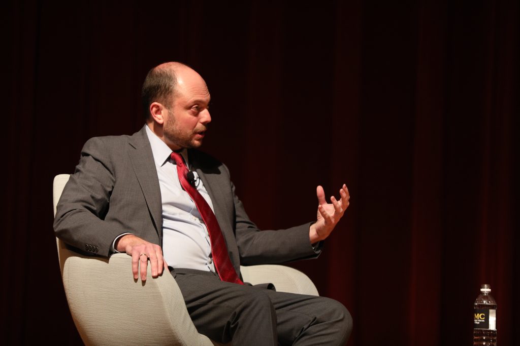 An individual in formal attire seated in a chair.
