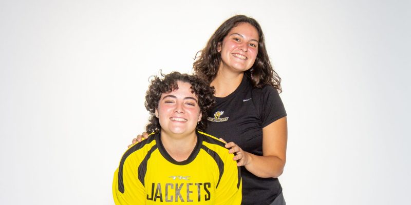 Two people pose together in front of a white background, one in a yellow "JACKETS 54" jersey, the other in black athletic wear.