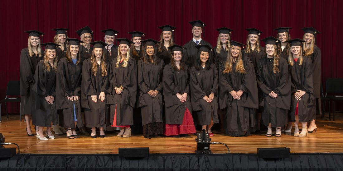 Graduates pose for a photo on stage in front of a red curtain.