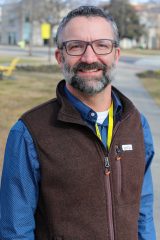 Person outdoors, smiling at the camera in a collared shirt and vest.