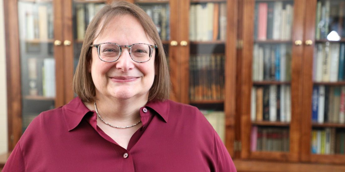 Person standing and smiling in front of a bookshelf filled with books.