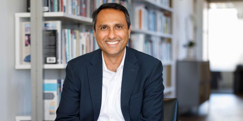 Person smiling while seated in a modern office, with bookshelves in the background.