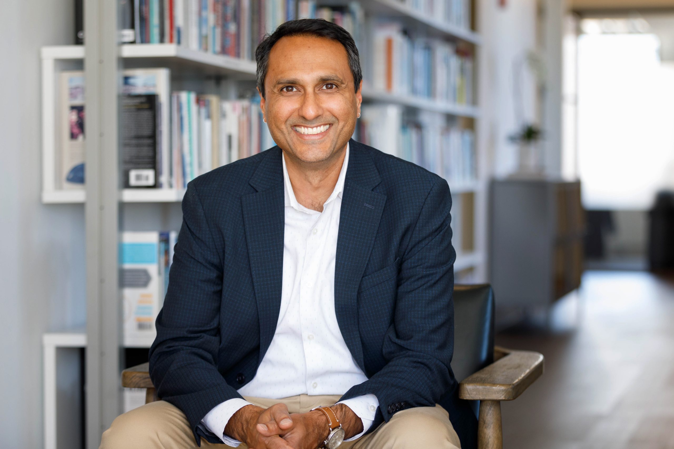 Person smiling while seated in a modern office, with bookshelves in the background.