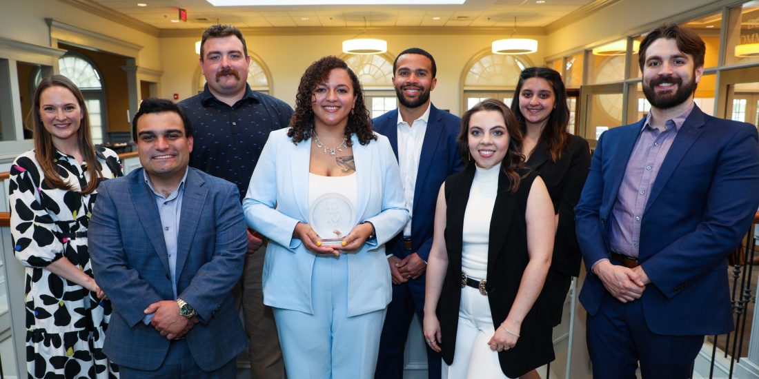 Eight 10 Under 10 awardees pose together smiling in the atrium on the second floor of Brock Commons