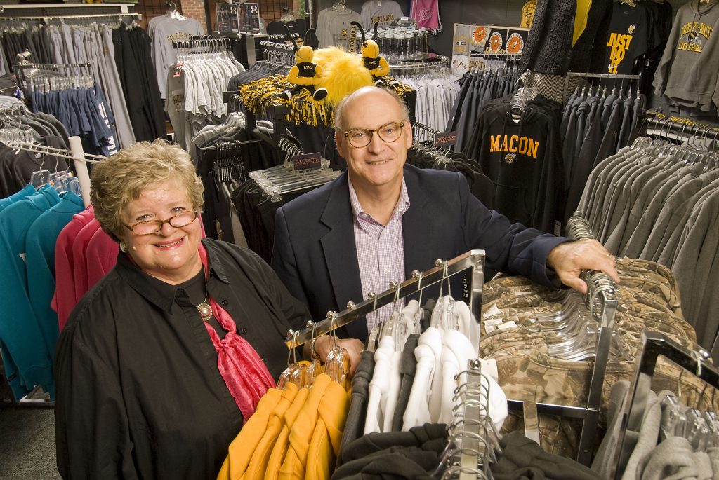 A couple stands smiling among racks of clothes and Randolph-Macon gear in a store