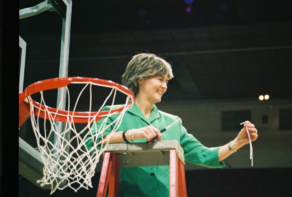 Carroll LaHaye stands atop a ladder, holding a piece of a basketball net that she's cut down