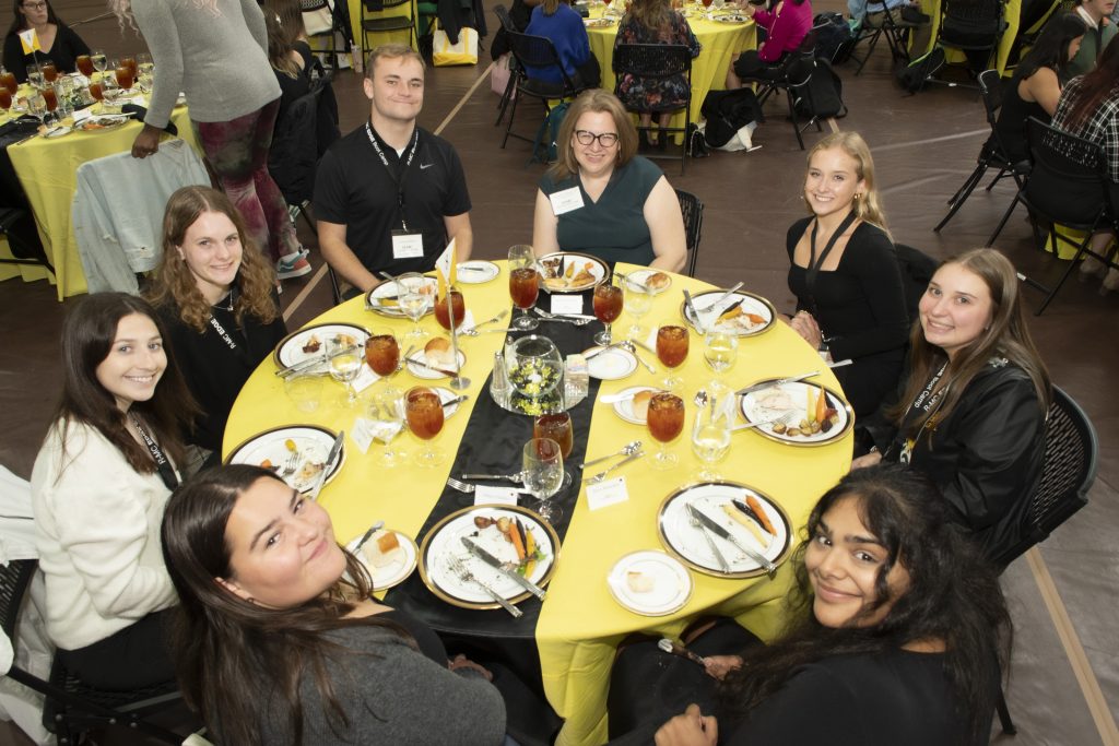 RMC students and an Edge Boot Camp volunteer sit around a circular table during an etiquette dinner with plates of food