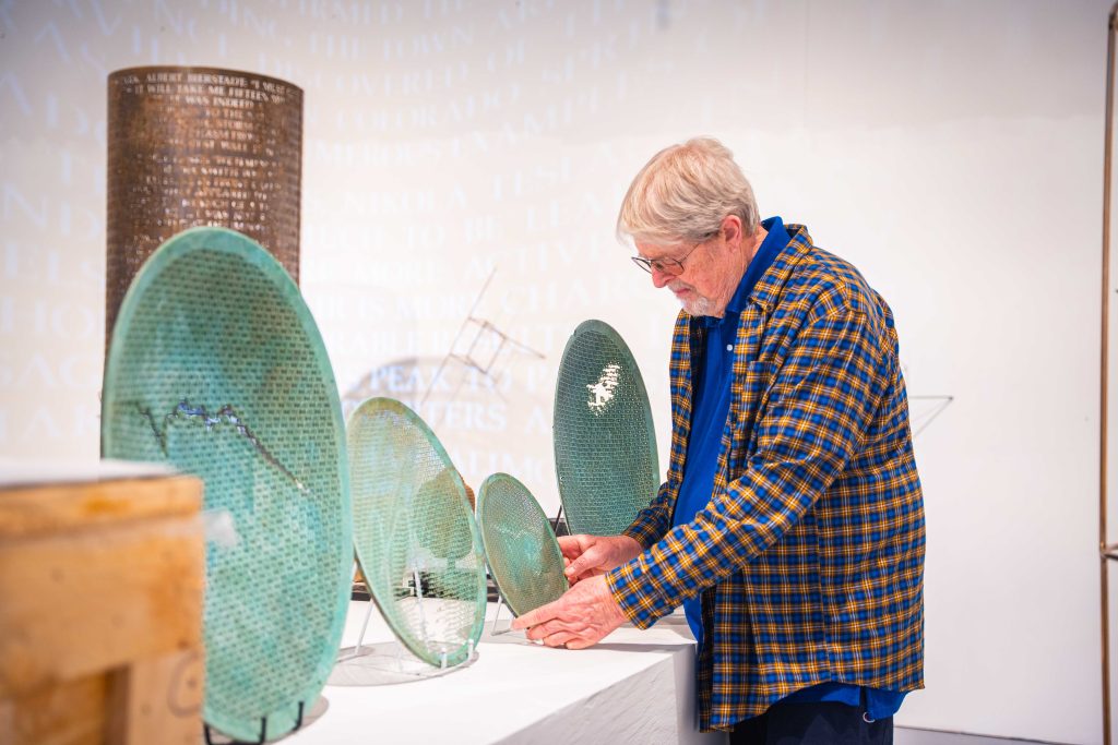 Jim Sanborn adjusts green copper sculptures on display stands inside his studio
