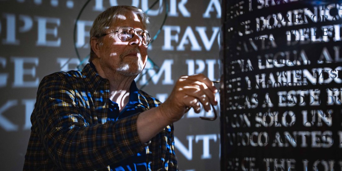 With illuminated text cast on the walls and himself, Jim Sanborn uses a tool on a cylinder sculpture