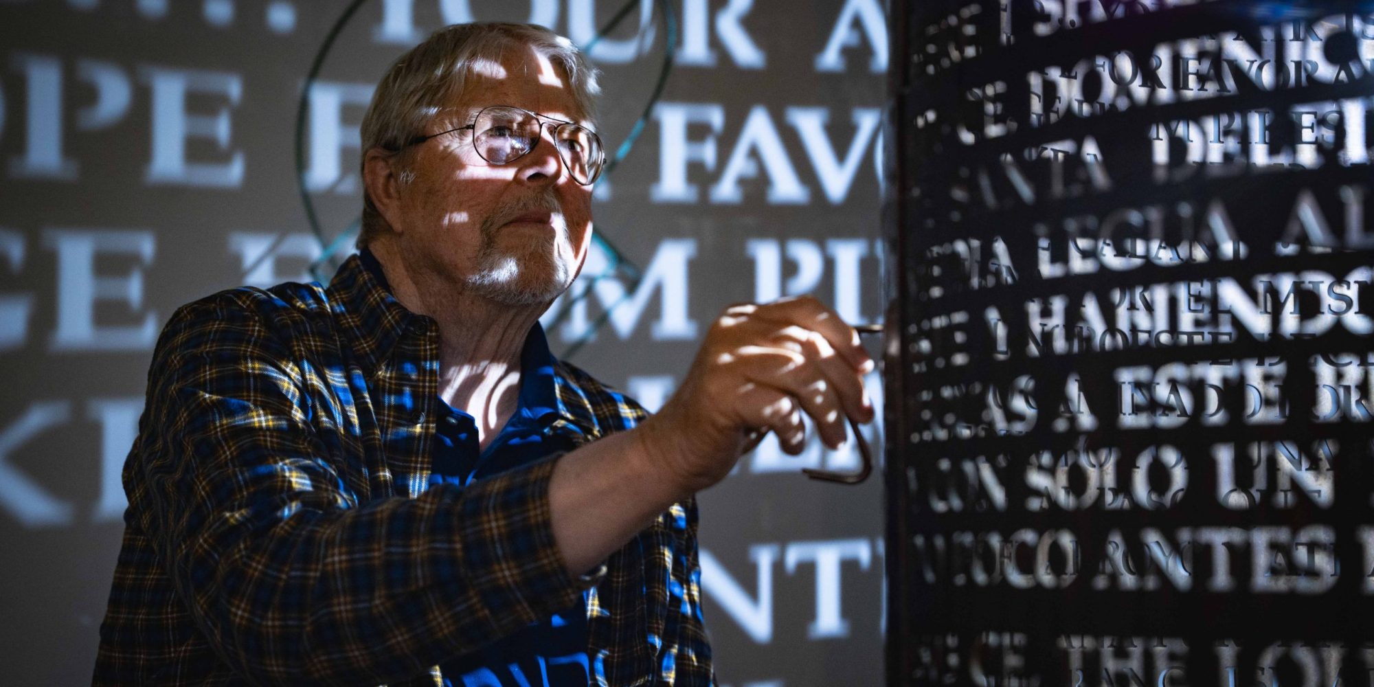 With illuminated text cast on the walls and himself, Jim Sanborn uses a tool on a cylinder sculpture