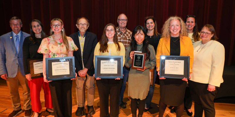 The winners of prestigious faculty and staff awards stand on the Blackwell Auditorium stage between President Michael Hill and Provost Alisa Rosenthal