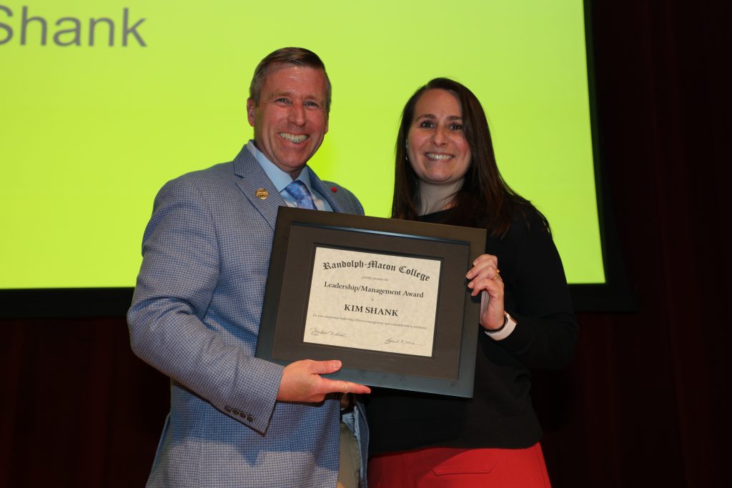 Kim Shank and President Michael Hill stand on the Blackwell stage holding a certificate