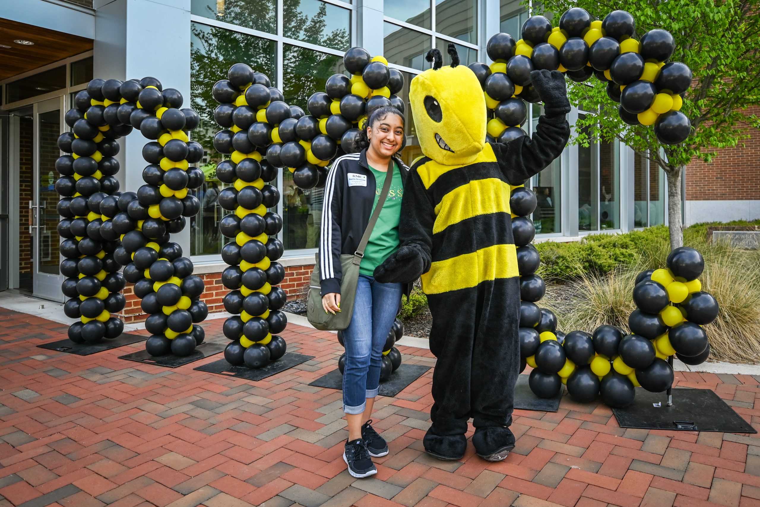 An admitted student poses with Buzz - the College's Yellow Jacket mascot - in front of balloon letters spelling RMC