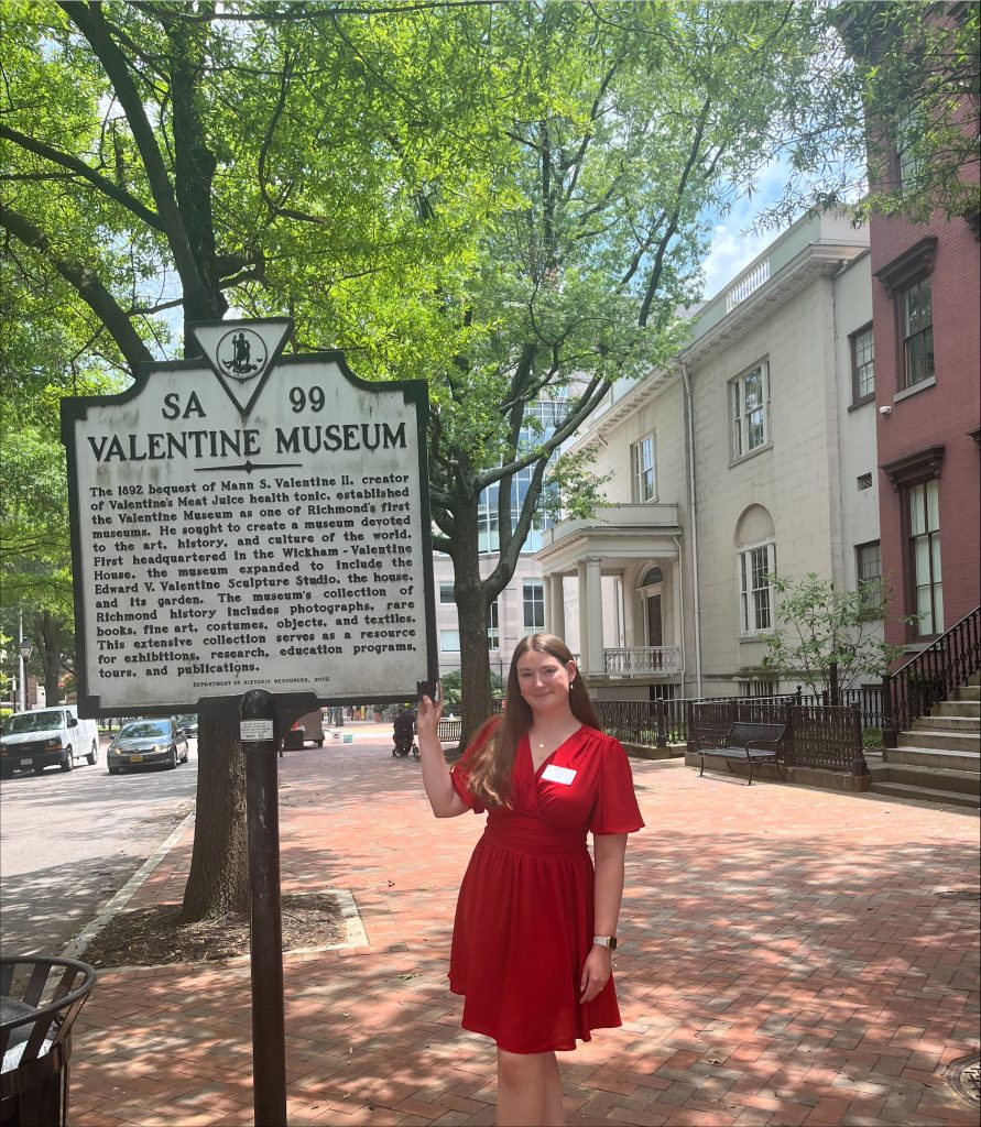 An RMC student stands on a Richmond sidewalk next to a historical marker for the Valentine Museum