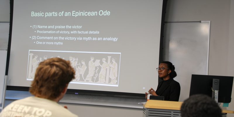 An RMC professor stands at the front of a classroom giving instruction on Epinicean Ode